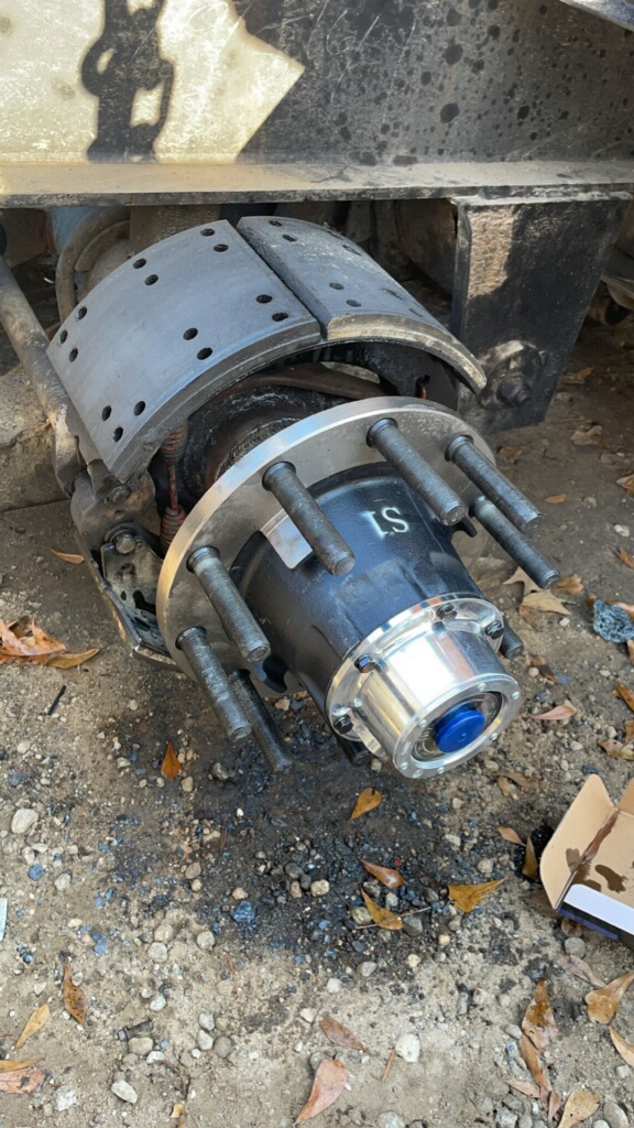 A truck axle with the brake shoes and a new hub with studs mounted