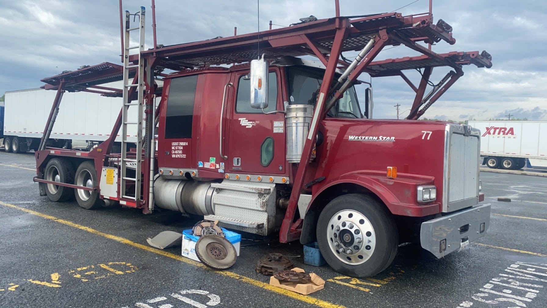 A car hauler parked in a truck lot with its clutch and flywheel laid out on the pavement